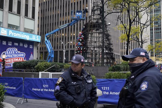 Police officers in the foreground of the partially burned out Fox News Christmas tree, with a worker on a cherry picker in the background removing the ornaments
